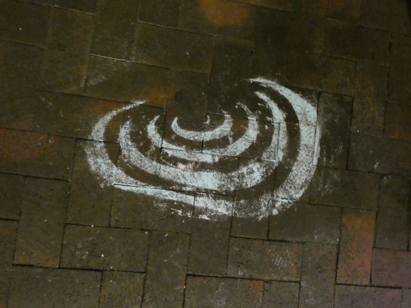 A white chalk spiral drawn on dark sidewalk pavers