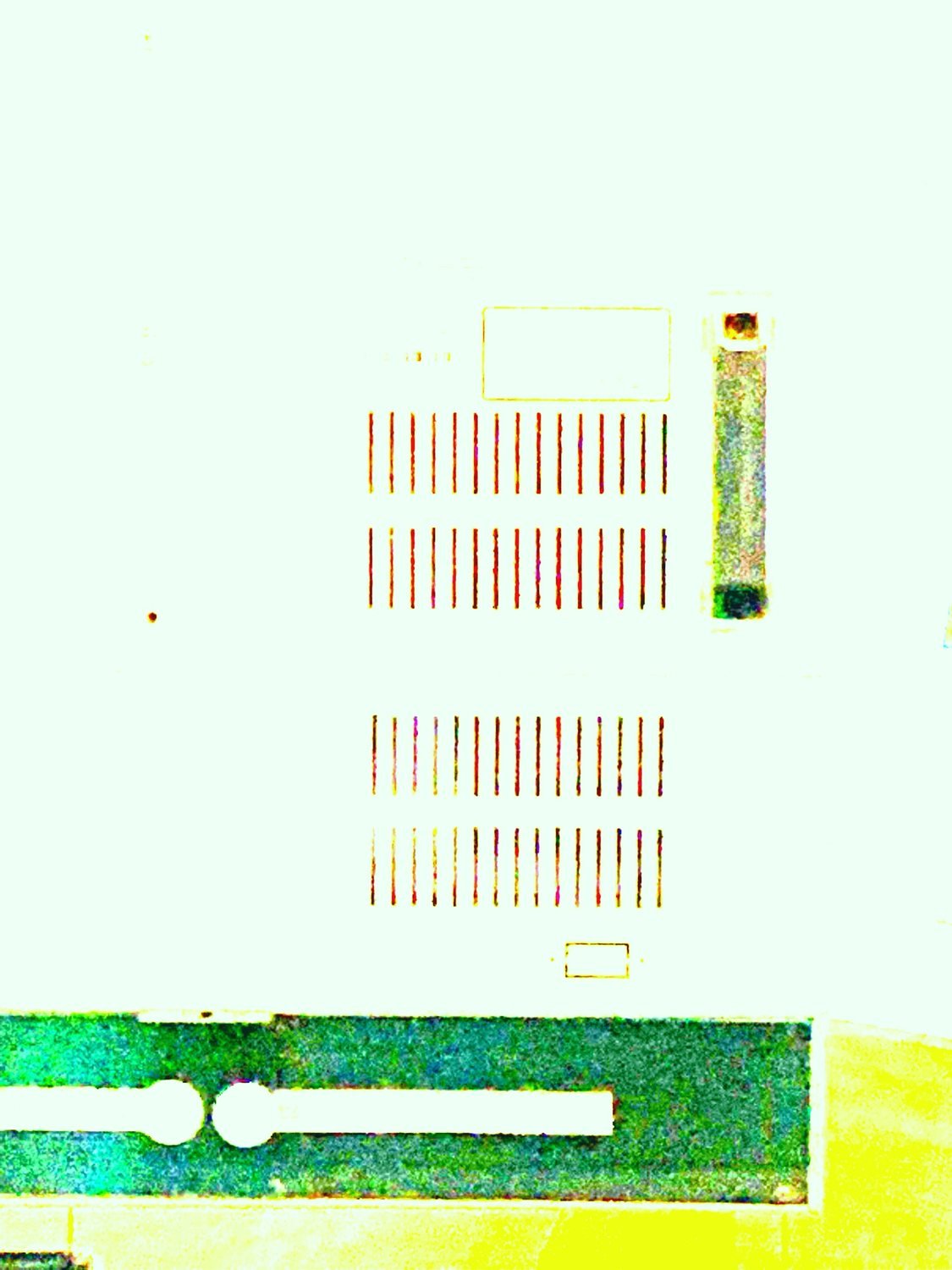 Overexposed close-up of a device panel with rows of thin red vent slots on a pale ground