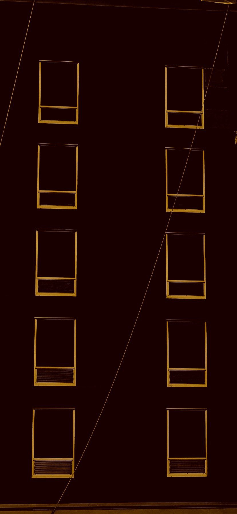 The face of a dark building with two columns of window frames picked out in amber, a single cable slanting across