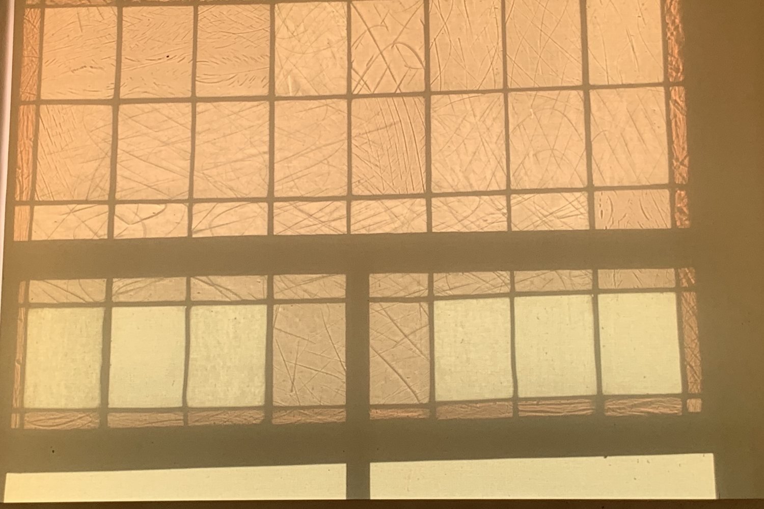 Warm light through a leaded window with scratched panes, dark lead lines forming a grid